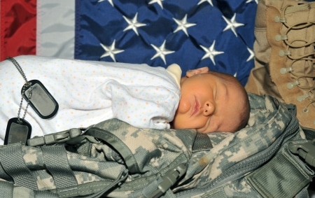 A decorative image of a newborn baby laying on a soldier's fatigues and dogtags. 
