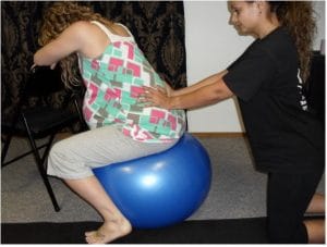 A Madriella student demonstrates how to massage the lower back while the client is sitting on a birth ball.