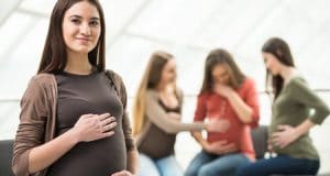 beautiful pregnant woman is looking at the camera. happy pregnant women are talking together at antenatal class at the hospital on background.