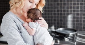 A new mother holding an infant in the kitchen