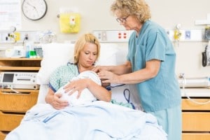 mature female nurse assisting woman in breast feeding newborn baby in hospital room