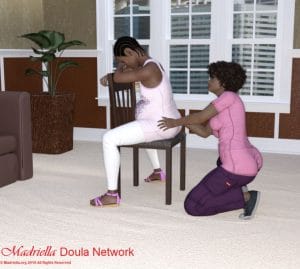 A pregnant woman sitting backwards on a chair while a Doula massages her lower back